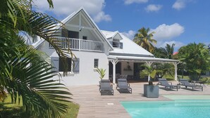 A two-story house with a covered patio area and a swimming pool. - In the heart of the island, with a view of the sea, near the rivers, 2 minutes from the Vallombreuse Garden (PETIT-BOURG)