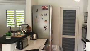 A kitchen with a refrigerator, toaster, and a glass jar with apples. - In the heart of the island, with a view of the sea, near the rivers, 2 minutes from the Vallombreuse Garden (PETIT-BOURG)