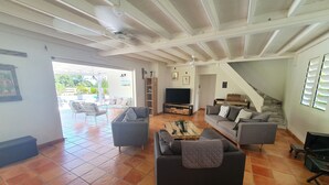 A spacious living area with a large TV, multiple sofas, a coffee table, and a staircase leading to an upper level. - In the heart of the island, with a view of the sea, near the rivers, 2 minutes from the Vallombreuse Garden (PETIT-BOURG)