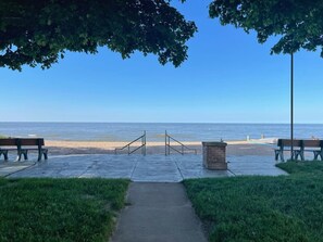 A paved walkway leading to a beach with benches and a trash bin. - Beachside Cottage- 1 min walk to sand and sun (Huron)