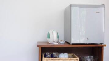 A compact kitchenette with a modern refrigerator, a kettle, and a wicker basket containing glasses and dishes.