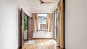 Un pasillo con suelo de madera, ventilador de techo y una ventana con cortinas.