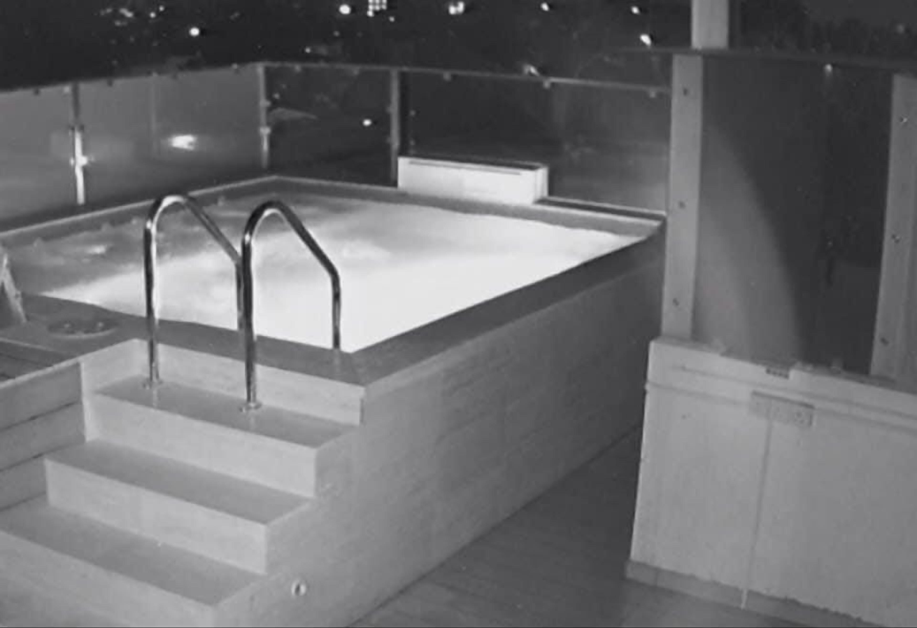 A rectangular pool with steps leading up to it, surrounded by a glass enclosure.
