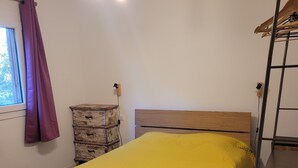 Una camera da letto con una testiera in legno, una coperta gialla con texture, un comò in legno e una scala in metallo.