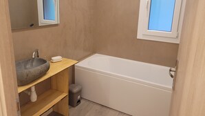 Un bagno moderno con un lavabo in pietra, una vasca da bagno bianca, un mobile vanitario in legno e una finestra vista.