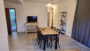 Zona pranzo con tavolo e sedie in legno, TV su un supporto e una libreria.
