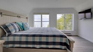 Quarto com uma cama grande, duas janelas e uma TV fixada na parede.