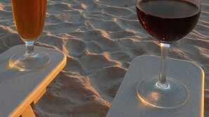 Två glas med dryck står på ett bord vid stranden, med en solnedgång i bakgrunden.