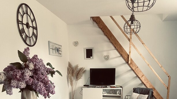 Una sala de estar moderna con una escalera de madera, un televisor de pantalla plana, un sofá y un comedor con una mesa y sillas.