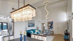 Een moderne keuken met een groot schiereiland, een eetgedeelte met een donker houten tafel, en een woonkamer met een blauwe bank en abstracte kunst.