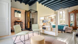 A spacious room with a herringbone-patterned wall, a large mirror, a wooden cabinet, a bookshelf, a bed with a green blanket, and a window with curtains. - Chateau / Country House (La Celle)
