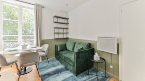 A modern living room with a green sofa, a small round table, and a whiteboard on the wall.