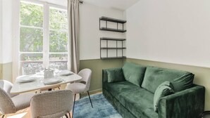 A compact living space with a dining area, a green sofa, and two wall-mounted shelves.