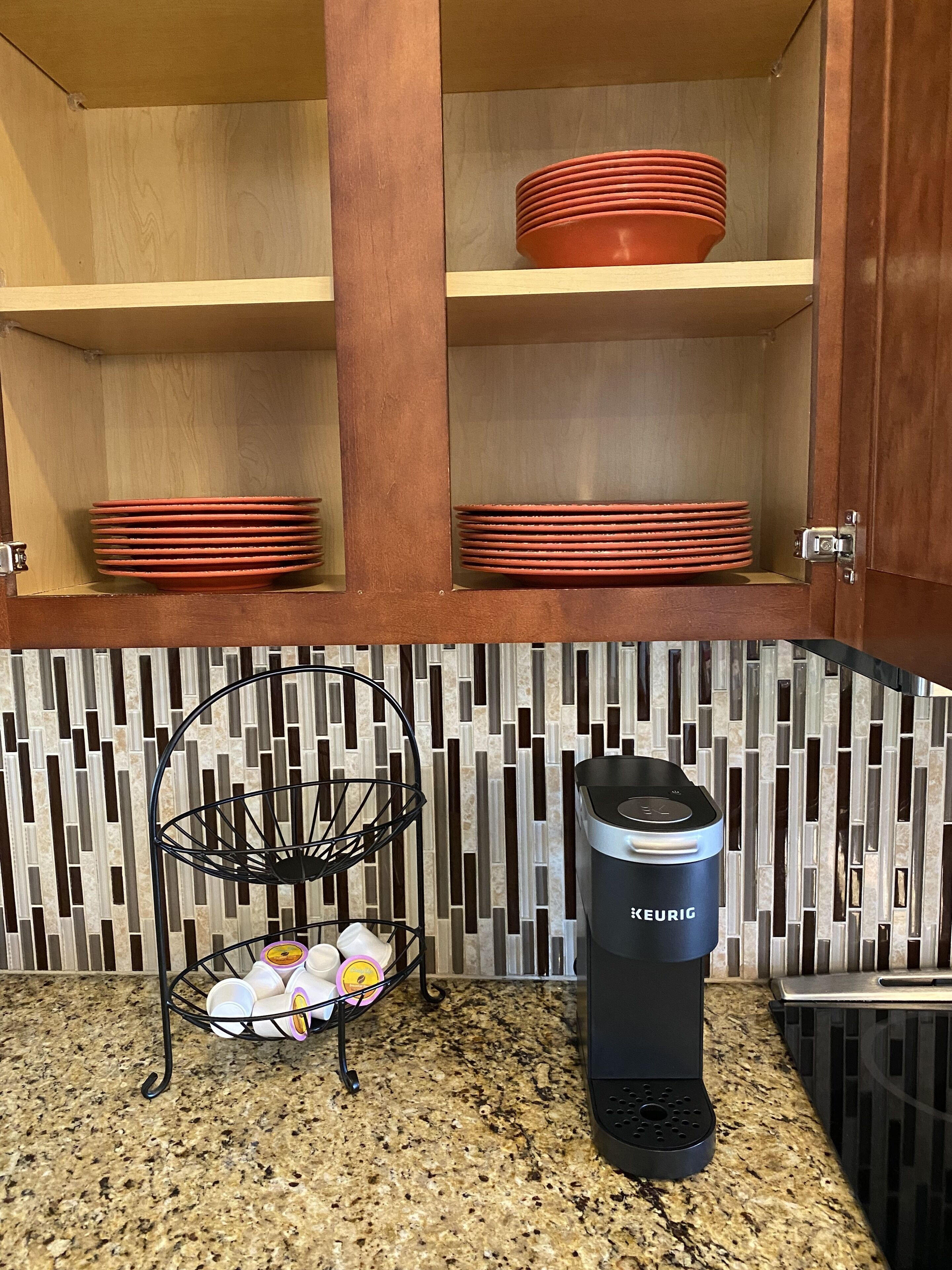 A kitchen with a coffee maker, stacked plates, and a dish rack.