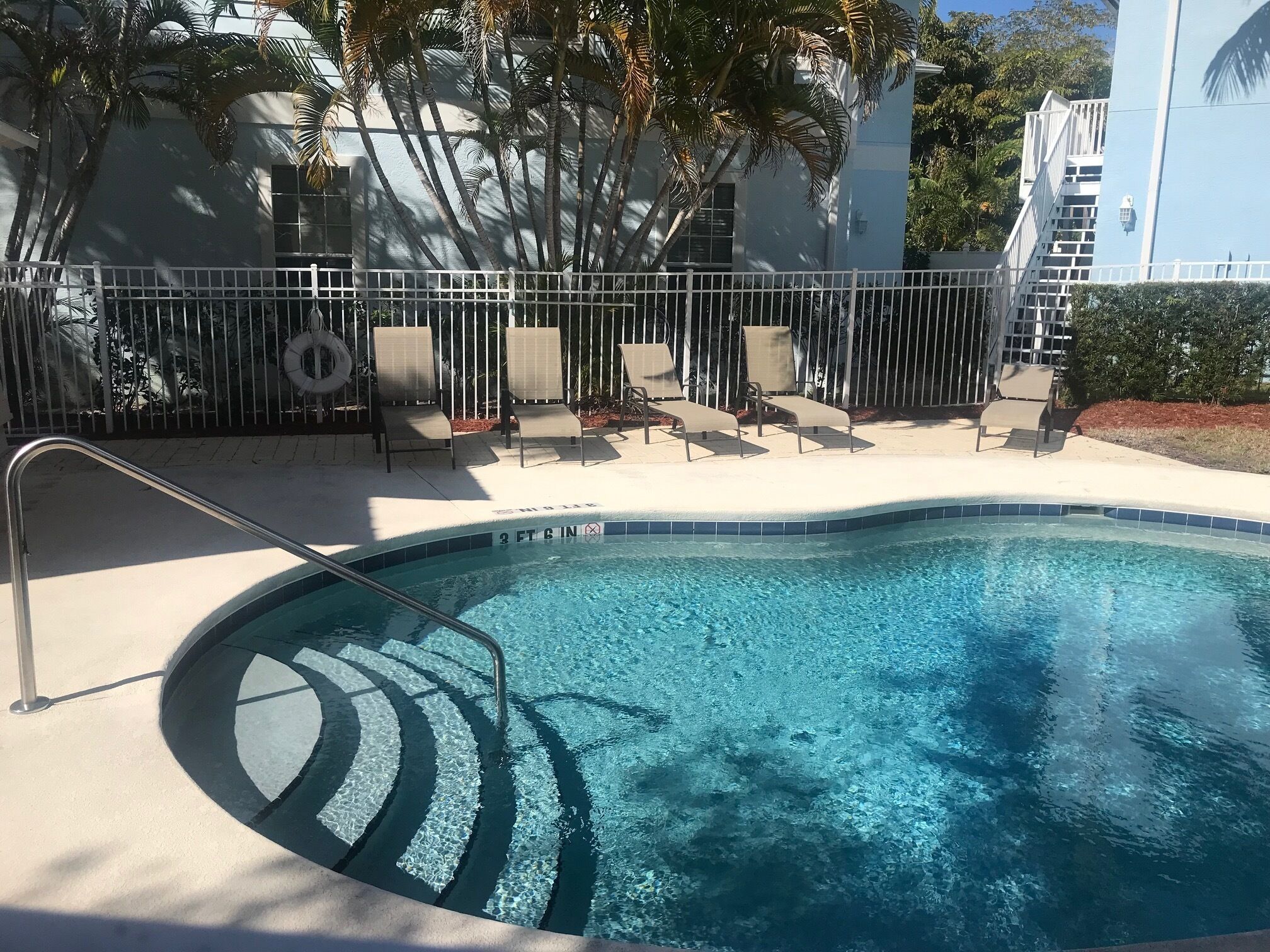A swimming pool with a metal ladder and lounge chairs.