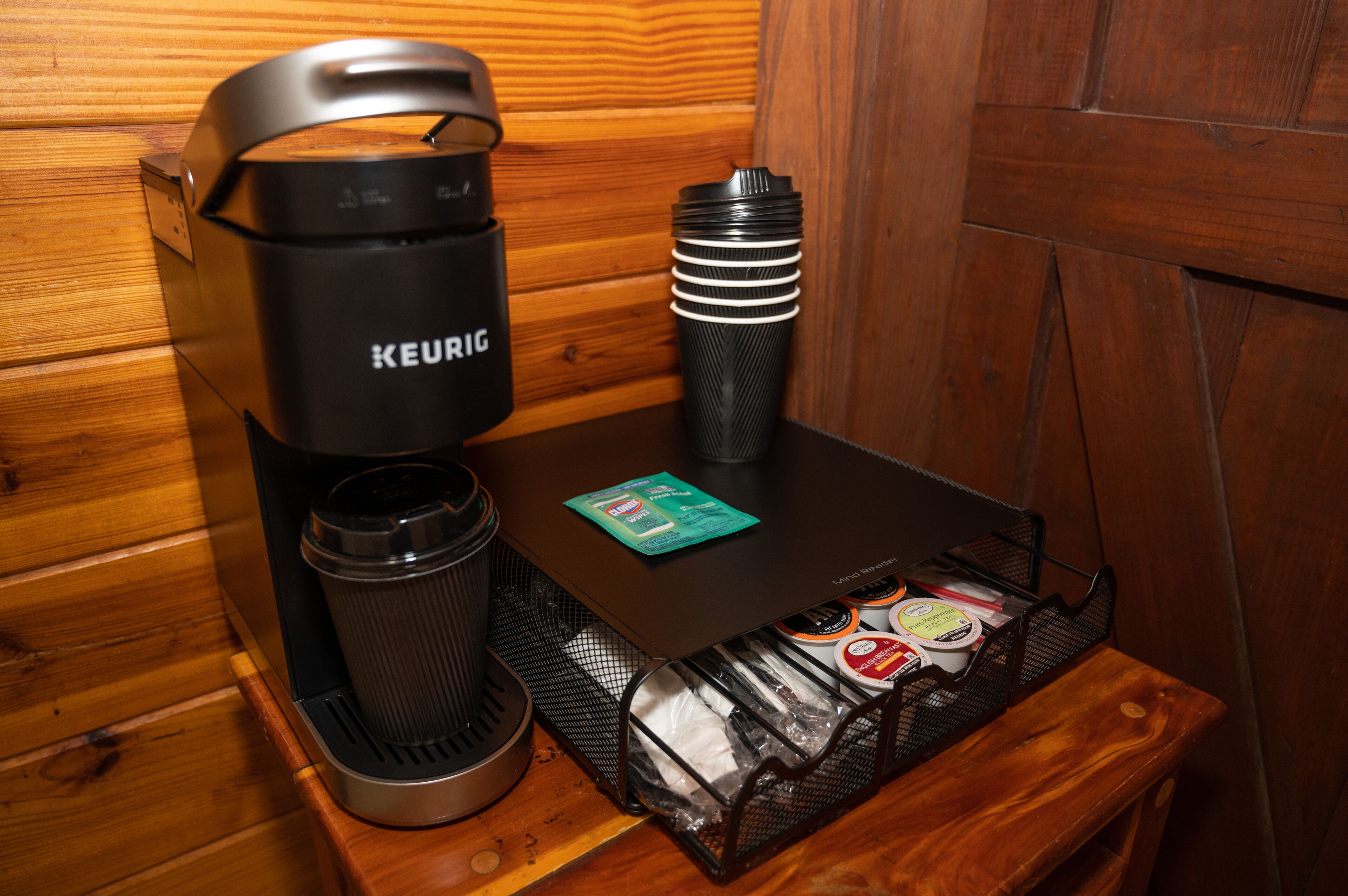 Keurig-kahvinkeitin, vesipullo ja kahvikapselihylly puisella pöydällä mökissä.