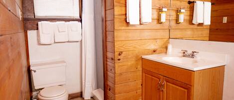 A wooden-paneled bathroom with a toilet, sink, and wooden cabinets.