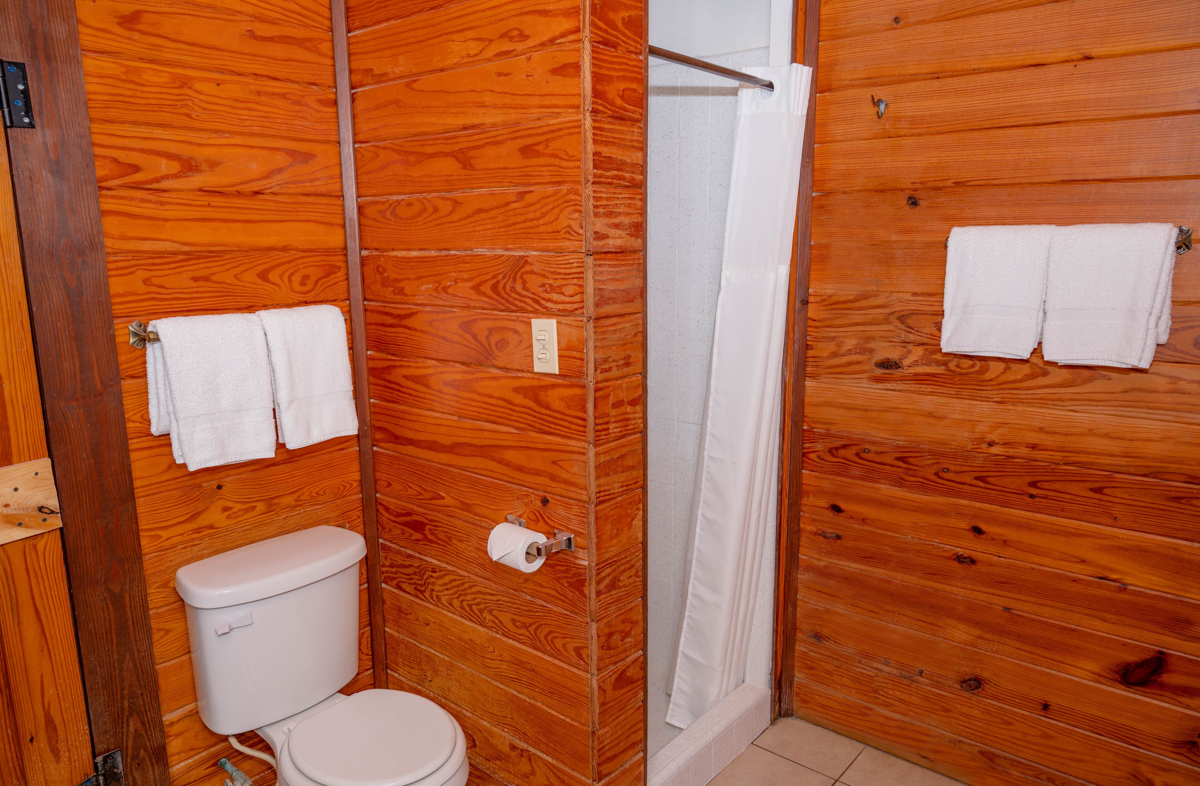 A wooden-paneled bathroom with a toilet, a shower, and two towels hanging on the wall.