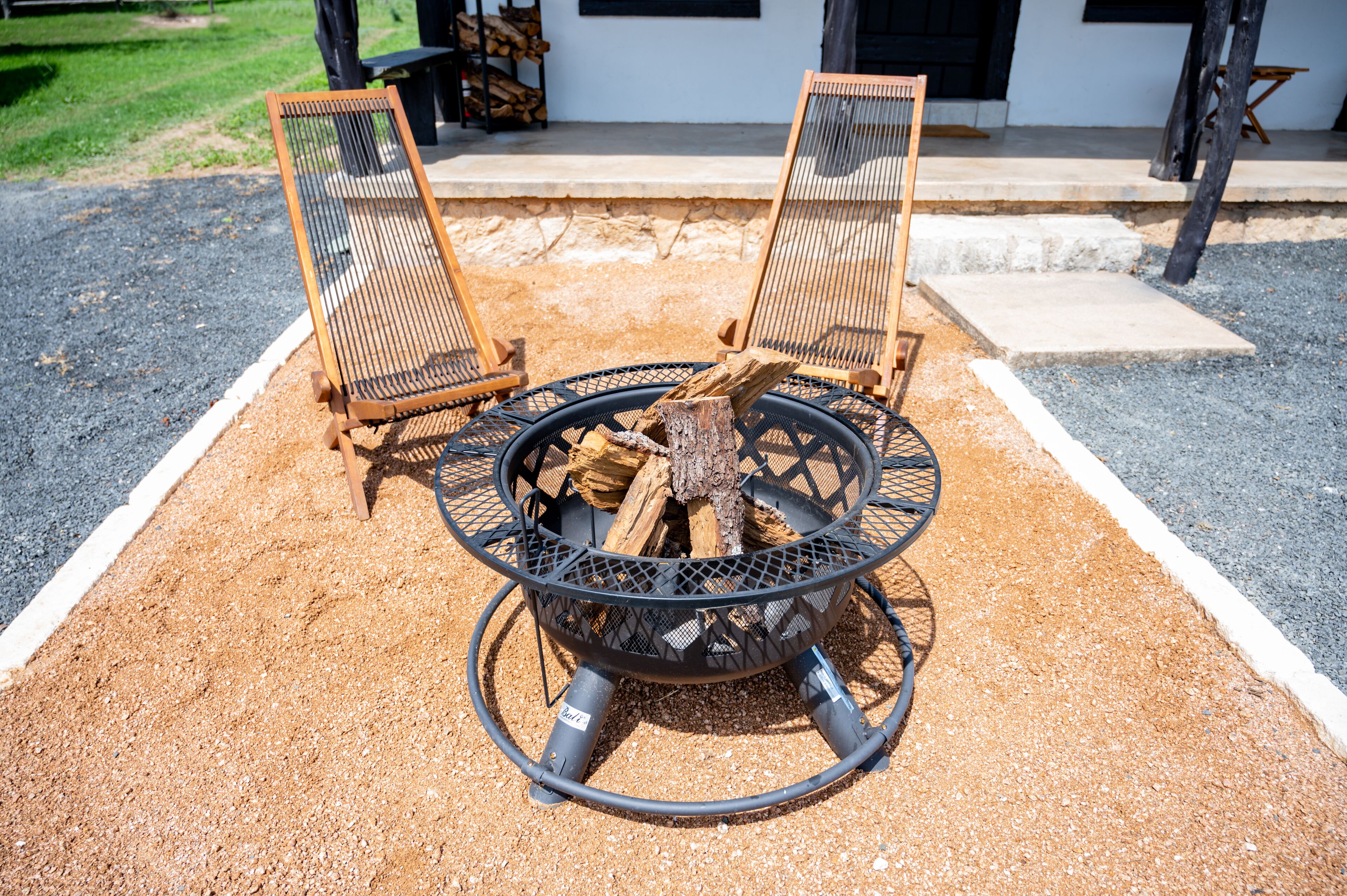 A fire pit with logs, surrounded by two wooden chairs.