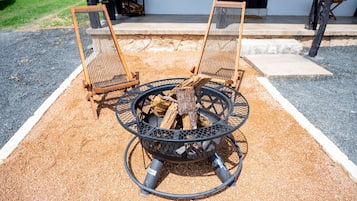 A fire pit with logs, surrounded by two wooden chairs.
