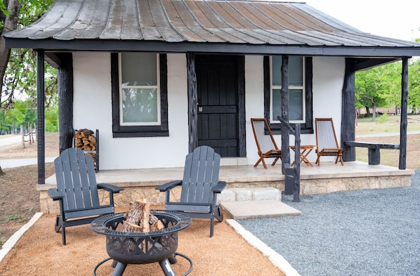 A rustic cabin with two Adirondack chairs, a fire pit, and a covered porch. - The Vaquero Motel (Bandera)