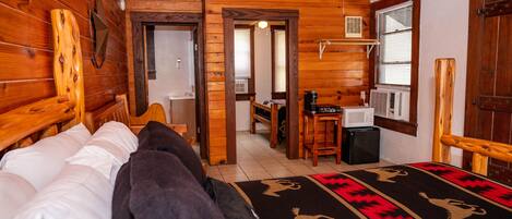 Una baita di legno con un letto, una scrivania e un bagno parzialmente visibile attraverso una porta aperta.