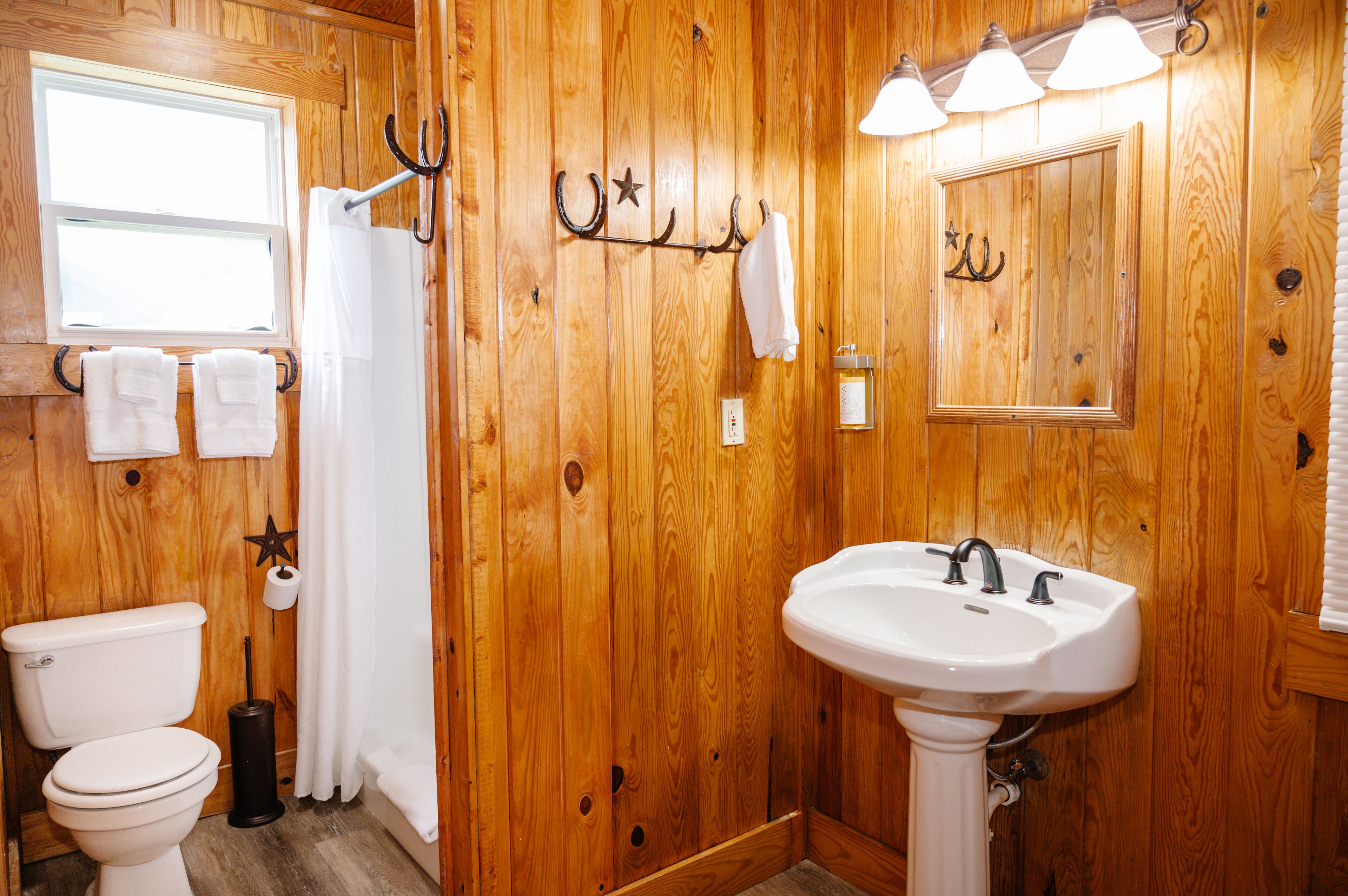 A wooden-paneled bathroom with a toilet, sink, and towel rack.