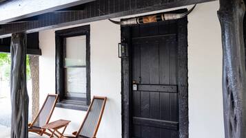 A building with a black door and windows, two wooden chairs outside, and a tree to the left.