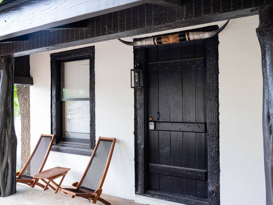 A building with a black door and windows, two wooden chairs outside, and a tree to the left.