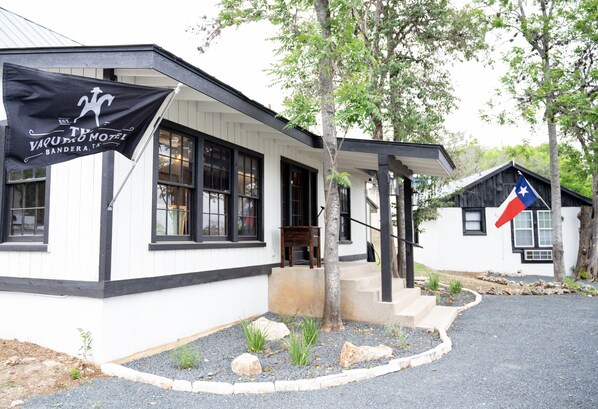 A building with a black and white exterior, a flag, and a Texas state flag. - The Vaquero Motel (Bandera)