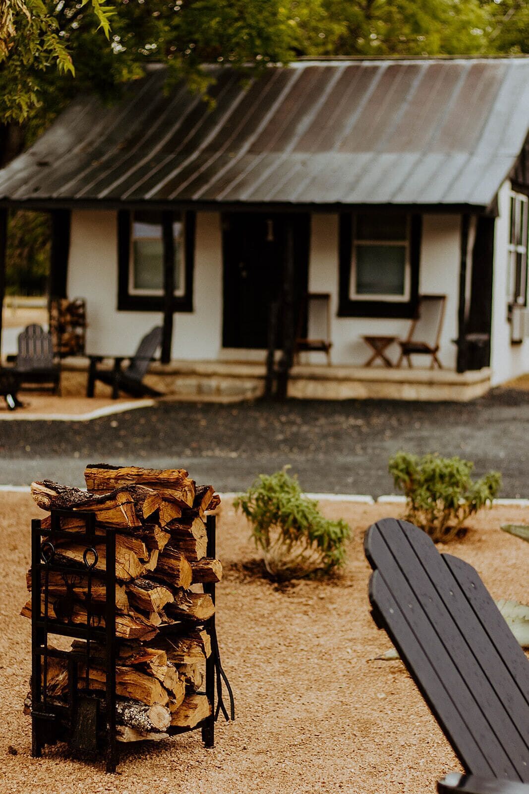 A rustic cabin with a metal roof, a stack of firewood, and a bench.