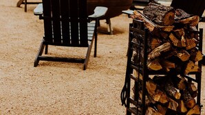Outdoor seating with Adirondack chairs, a wooden barrel, and a stack of firewood. - The Vaquero Motel (Bandera)