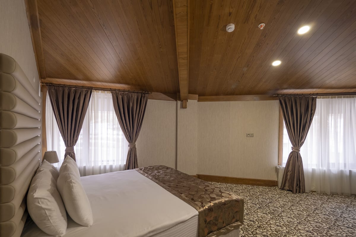 Un dormitorio con cama, cortinas, techo de madera y alfombra estampada.