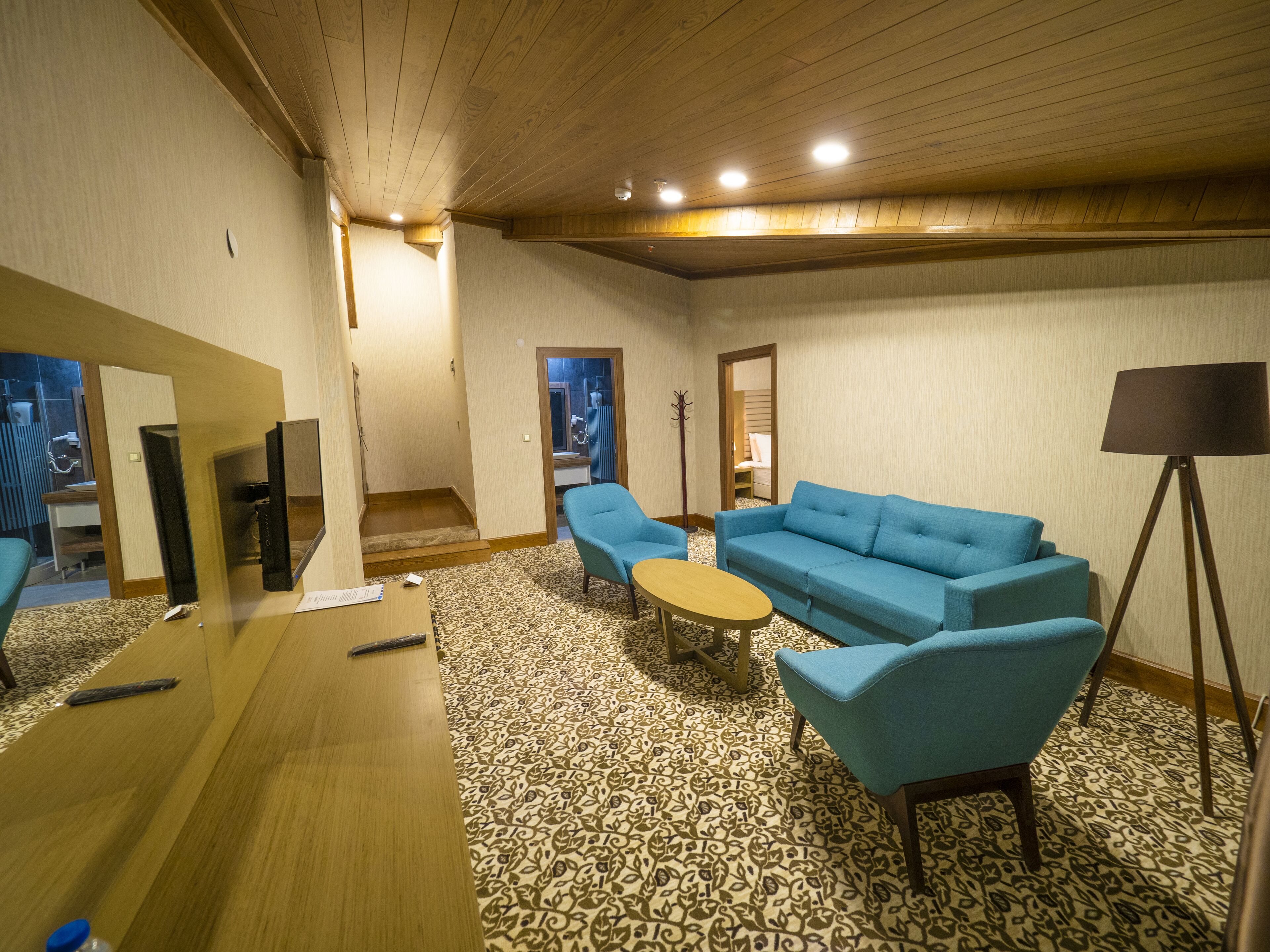 A hotel room with a wooden ceiling, a patterned carpet, a blue sofa, a small round table, and a floor lamp.