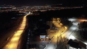 A nighttime aerial view of a cityscape with illuminated roads, a large building with a prominent sign, and distant city lights.