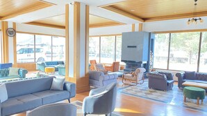 A spacious lobby with a large seating area, a fireplace, and large windows offering a view of the outside. - Balsoy Mountain (Erzurum)