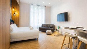 Une chambre d’hôtel moderne équipée d’un lit, d’un canapé, d’une petite table avec une chaise et d’un téléviseur fixé au mur.