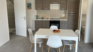 Eine moderne Küche mit weißem Esstisch und Stühlen, einem eingebauten Ofen und einer kleinen Kücheninsel mit Obstschale.