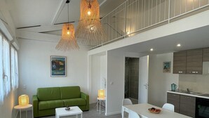 Ein modernes Wohnzimmer mit einem grünen Sofa, einem weißen Esstisch und Pendelleuchten.