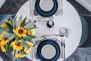 A round dining table with two blue plates, silver cutlery, and a vase of yellow flowers. - Fresh house, amazing location, great for couples! (Chester)