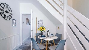 A dining area with a round table, four chairs, a vase of sunflowers, and a clock on the wall. - Fresh house, amazing location, great for couples! (Chester)