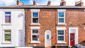 A two-story brick house with a red door, white-framed windows, and a small front garden. - Fresh house, amazing location, great for couples! (Chester)
