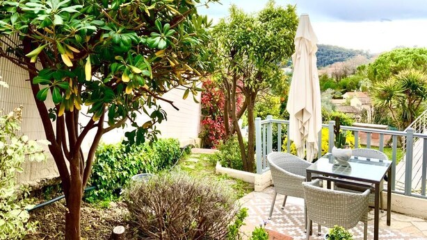 An outdoor patio with a table and chairs, surrounded by lush greenery and a view of the countryside. - Duplex house with garden in the hills above Cagnes  (Cagnes-sur-Mer)