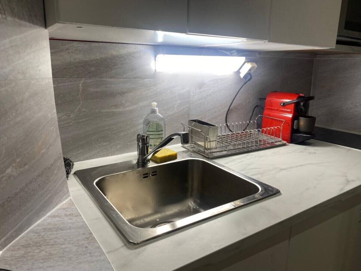 Un évier de cuisine en acier inoxydable, doté d’un distributeur de savon et d’une éponge, d’un égouttoir à vaisselle, et un appareil électroménager rouge en arrière-plan.