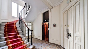 A grand staircase with red carpeted steps leading to a dark wooden door. - #Arc DeTriomphe #Trocadero #Style Haussmanien#AC (Paris)