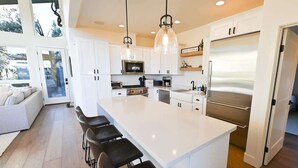 A modern kitchen with white cabinetry, a large island with bar stools, stainless steel appliances, and pendant lighting.