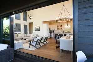 A modern living room with a sofa, chairs, and a dining table. There is a kitchen in the background with a chandelier. - OutWest Wapiti Rim Cabin (Pine)