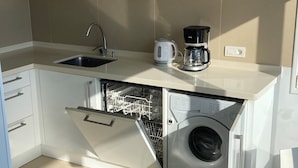 A compact kitchen with a dishwasher, a coffee maker, and a clock on the wall.