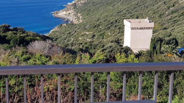 A coastal view with a white building on a hillside, overlooking the sea.