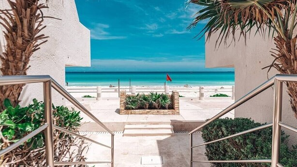 A staircase leading to a beach with a flag, palm trees, and a clear sky. - Villa Marlin, Cancun Caribe, Ocean front (Cancún)